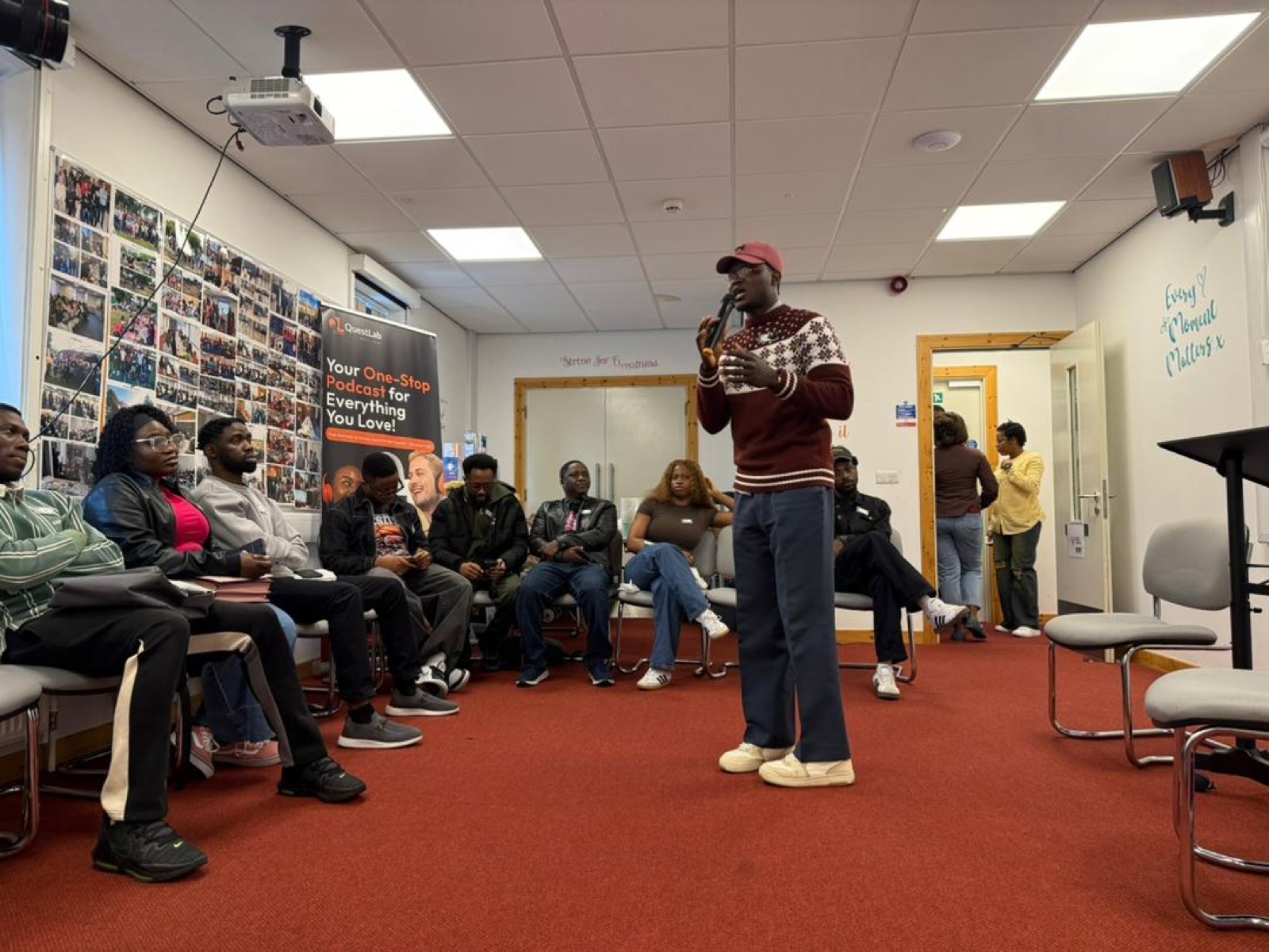 Oluwasegun Aluko James speaking into a microphone to a seated audience at a live TheQuestLab community event.